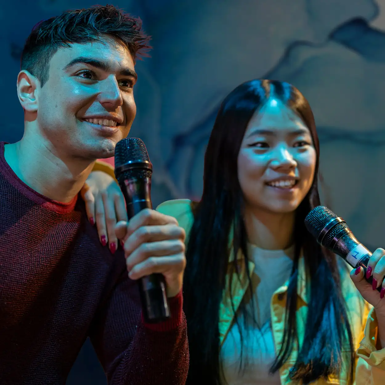 Smiling young man and woman holding microphones, enjoying karaoke together.
